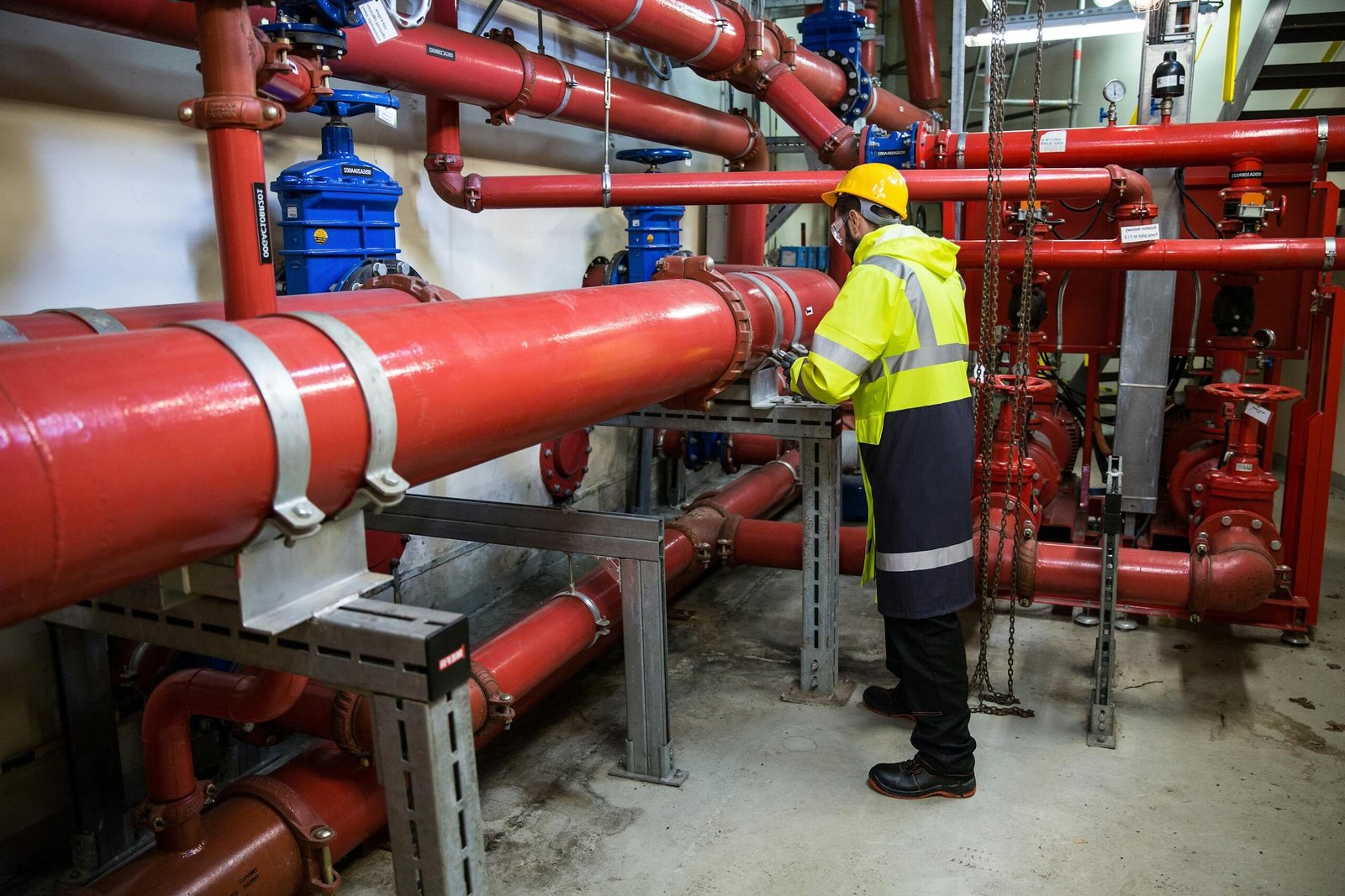Engineer with safety gear inspecting red industrial piping system indoors.